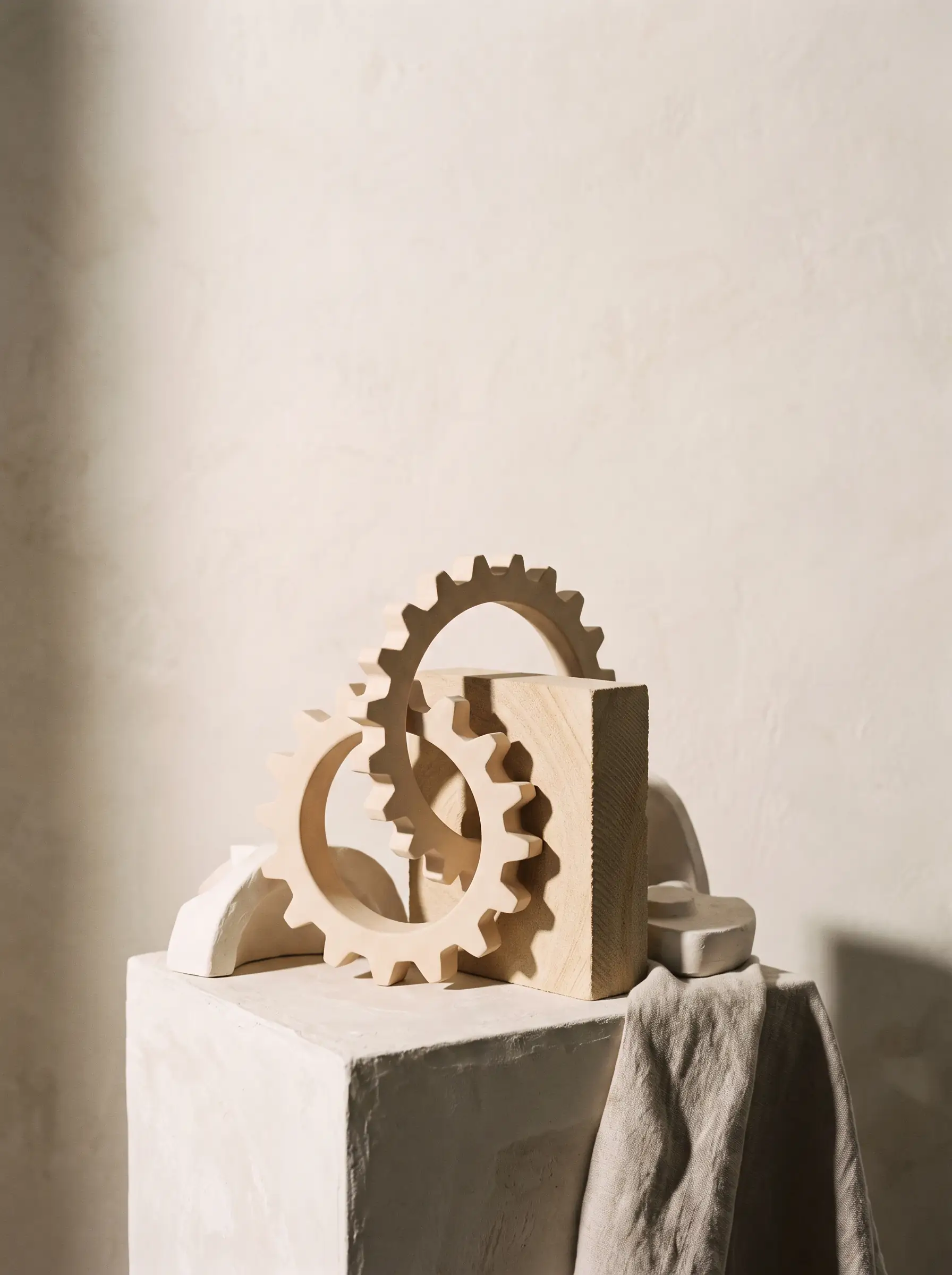 Editorial still-life for LASEO's Manufacturing SEO Agency page: interlocking pale ceramic gear-like rings and a machined sandstone block fitted together on a plaster pedestal